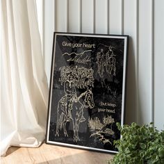 a black and white poster sitting on top of a wooden table next to a potted plant