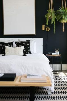 a bedroom with black walls, white bedding and plants hanging above the headboard