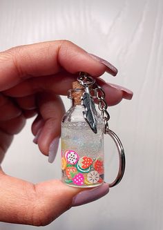 a hand holding a glass bottle with a feather charm on it's keychain