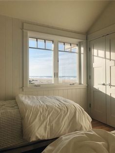 two beds in a room with white walls and wooden flooring, along with large windows that look out onto the beach