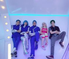 four people sitting on a white wall with their arms crossed and legs crossed, all wearing blue hair