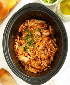 shredded chicken in a slow cooker with green onions and cilantro on the side