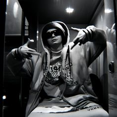 a man with sunglasses and a hoodie sitting on a bench in front of a mirror