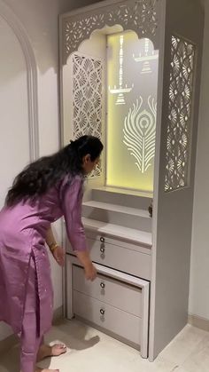 a woman in a purple dress standing next to a cabinet with drawers and doors on it