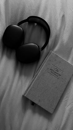 an open book, sunglasses and headphones on a white bed with a pair of black glasses