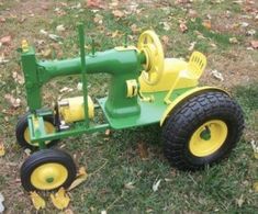 a green and yellow toy tractor sitting on top of a grass covered field next to leaves