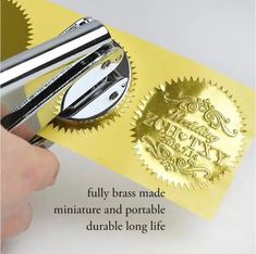 a person is cutting out a gold stamp on a piece of yellow paper with scissors