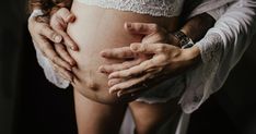 a pregnant woman's belly is being held by two hands while her husband holds her