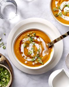 two bowls filled with soup and garnishes on a white tablecloth next to silverware