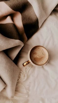 a cup of coffee sitting on top of a bed next to some blankets and pillows