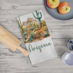 a kitchen towel with an arizona desert scene on it next to two apples and a knife