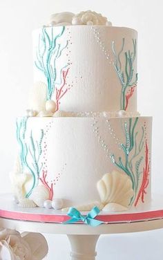 a three tiered cake decorated with sea shells and corals on a white table