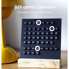 a black calendar sitting on top of a wooden table next to a yellow lamp and white wall