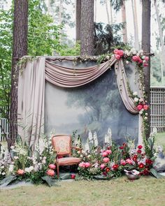 a chair sitting in the middle of a lush green field next to a wall covered with flowers