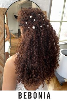 the back of a woman's head with long curly hair in front of a mirror