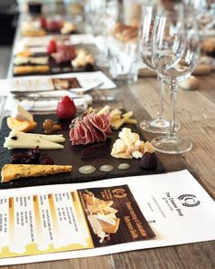 a wooden table topped with lots of different types of food and wine glasses on top of it