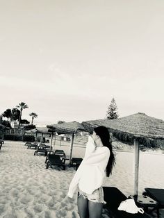 a woman standing on top of a sandy beach next to umbrellas and lounge chairs