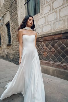 a woman in a white dress is standing on the sidewalk and looking off into the distance