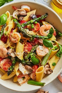 pasta with shrimp, asparagus and tomatoes in a white bowl on a table