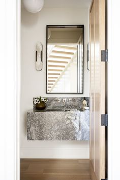 a bathroom sink sitting under a mirror next to a wooden door and light fixture on the wall