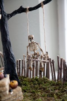 a skeleton sitting on a swing in front of a tree