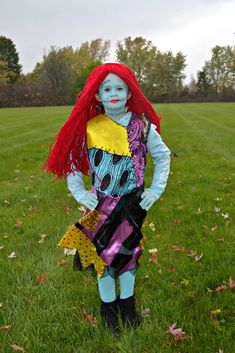 a child dressed up as the little mermaid with red hair and blue makeup standing in grass