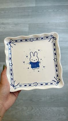 a hand holding a blue and white plate with a bunny on it