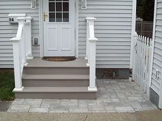 a white front door and steps leading to a house with brick pavers on the ground