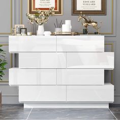 a white dresser sitting next to a wall with pictures on it's sideboard