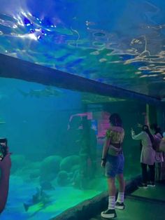 people standing in front of an aquarium looking at their cell phones as they take pictures