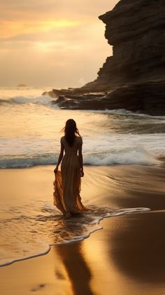 a woman in a long dress is walking on the beach at sunset with waves coming in