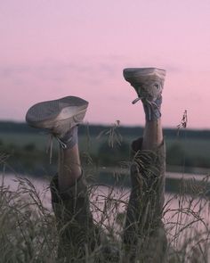 two legs with shoes on their feet in tall grass near the water at sunset or dawn