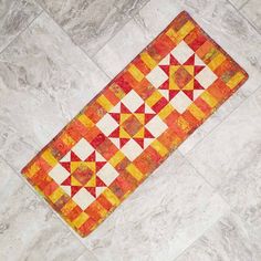 an orange and yellow quilt laying on the floor next to a white tiled flooring