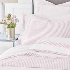 a bed with pink and white striped comforter next to a vase filled with flowers