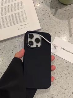 a person is holding an iphone case in their hand while sitting at a table with a book