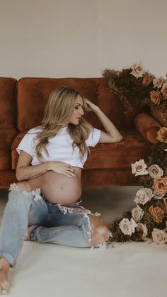 a pregnant woman sitting on the floor next to a couch with her hands behind her head