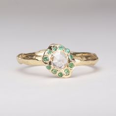 a close up of a gold ring with an oval shaped diamond and green stones on it