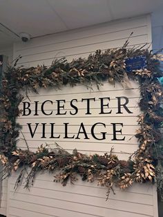 a sign that says bicester village on the side of a building with evergreens and pine cones