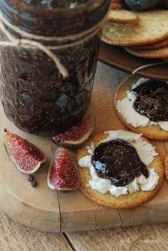 figs and crackers on a cutting board next to a jar of jam,