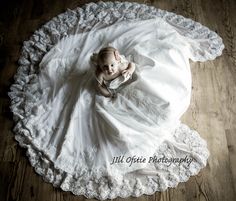 a baby in a white dress laying on a wooden floor with lace around it's edges