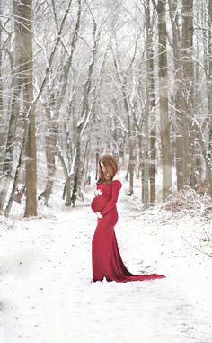 a woman in a long red dress standing in the snow with her hands on her hips