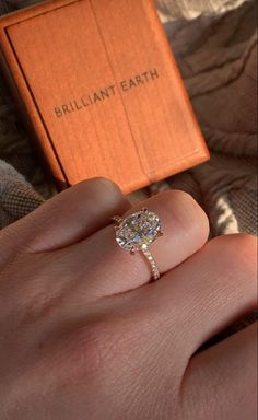 a woman's hand with a ring on it and an orange box in the background