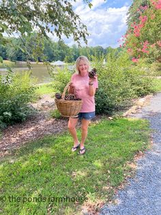 a woman holding a basket full of mushrooms in her hands while standing on the side of a road