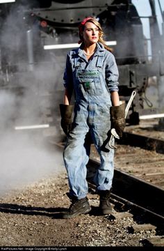 a woman in overalls standing next to a train