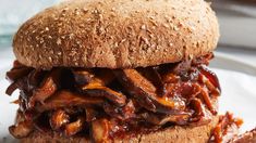 a close up of a sandwich on a plate with meat and sauce in the background