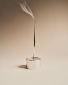 a small white vase with a long stick sticking out of it's side, on a plain surface