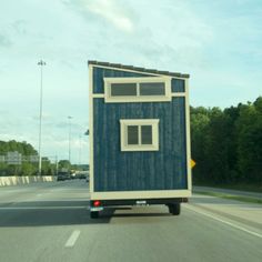 a blue and white tiny house is on the back of a truck driving down the road