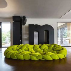 a large green bean bag chair sitting on top of a wooden floor in front of a giant letter