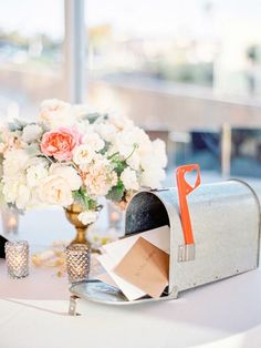 a white table topped with a mailbox next to a vase filled with pink and white flowers