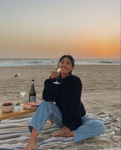 a woman sitting on top of a beach holding a glass of wine